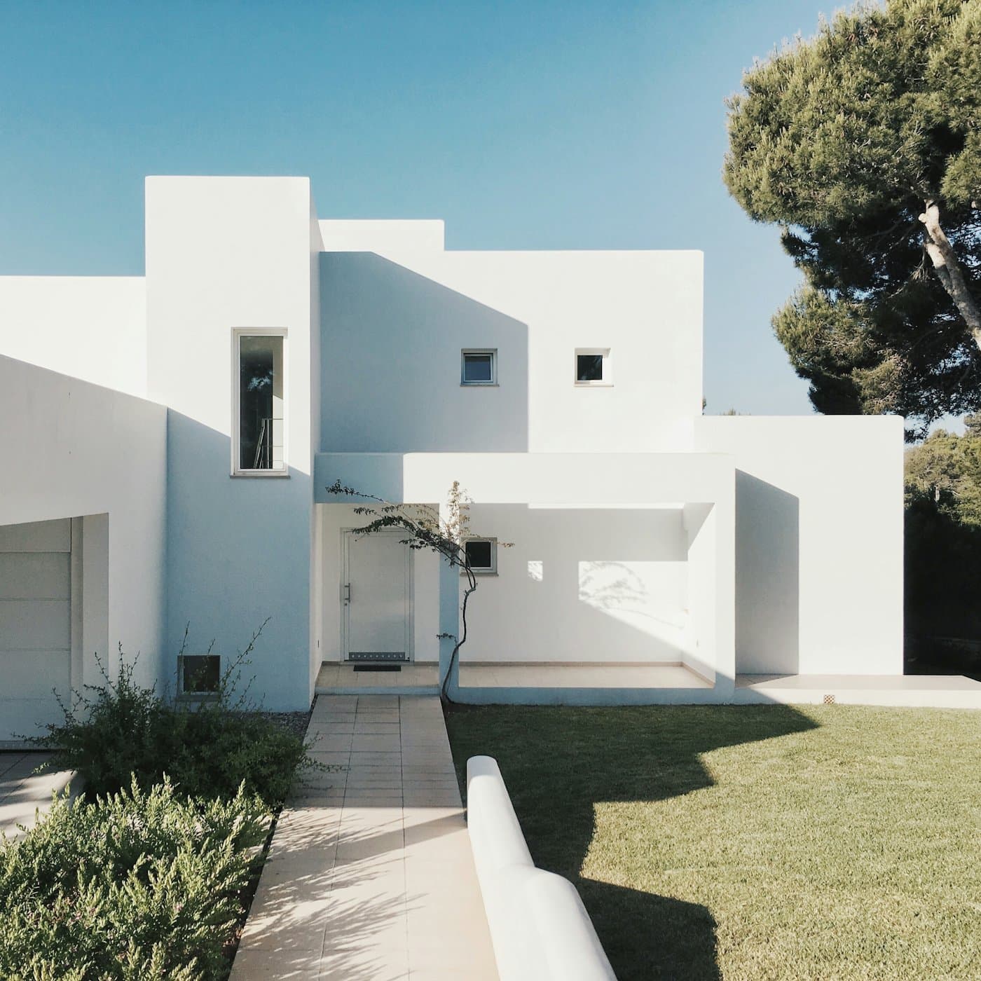 Villa contemporaine aux volumes blancs épurés, sous un grand pin et un ciel bleu